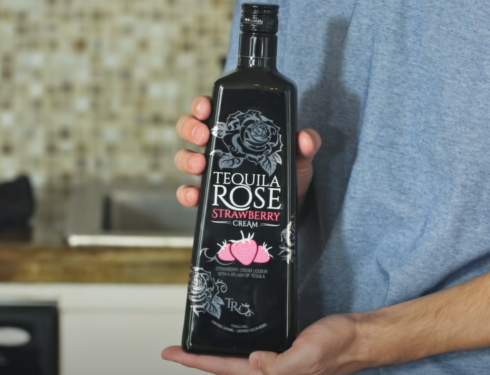 A man in a blue shirt holding a bottle of Tequila Rose