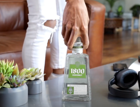 A man gripping the neck of a 1800 tequila bottle resting on a short table