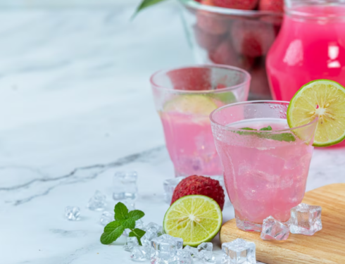 two pink cups with lime, ice cubes, and fruits on the table